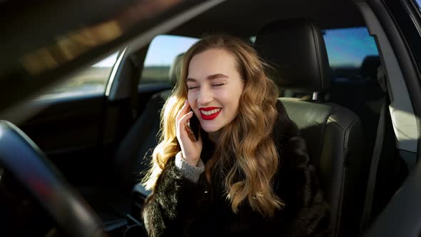 Cheerful Happy Beautiful Woman Talking on the Phone and Laughing Sitting in Car on Driver's Seat alt