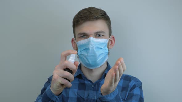 Man in protective medical mask spraying on hands antiseptic for protection from bacterias and virus alt