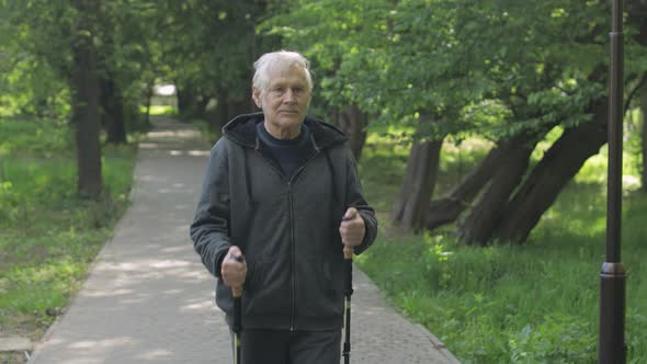 Active Senior Old Man Training Nordic Walking with Ski Trekking Poles in Park alt