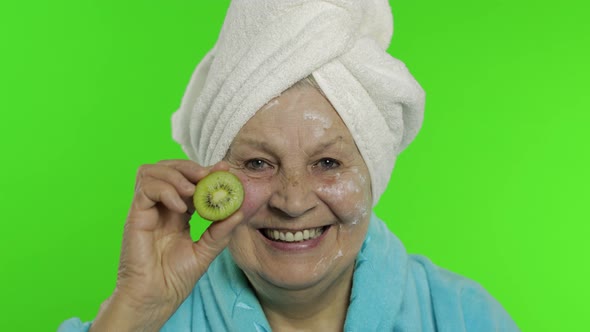 Elderly Grandmother in Bathrobe. Old Woman with Half of Kiwi in Her Hand alt