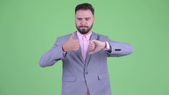 Confused Young Bearded Businessman Choosing Between Thumbs Up and Thumbs Down alt