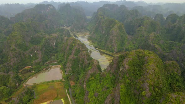 Aerial Shot of Beautiful Limestone Mountains with Passes Carved By a River in Ninh Binh Region a alt