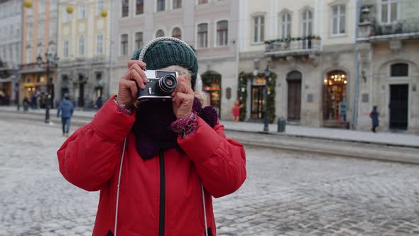 Senior Woman Tourist Taking Pictures with Photo Camera Using Retro Device in Winter City Lockdown alt