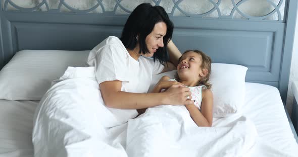 Woman with Her Little Daughter Speaking and Smiling Resting in the Bed in the Morning alt