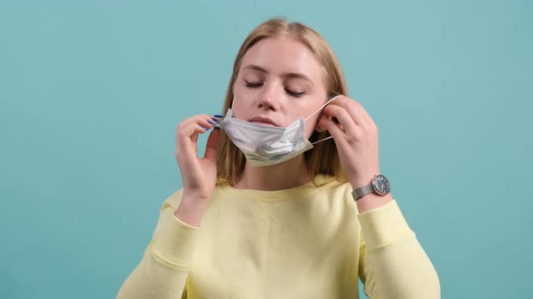 Young Woman Put on Medical Mask on a Turquoise Background. alt