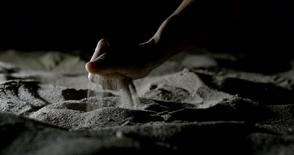 Person Takes Handful of Dry Sand and Holds in Darkness alt