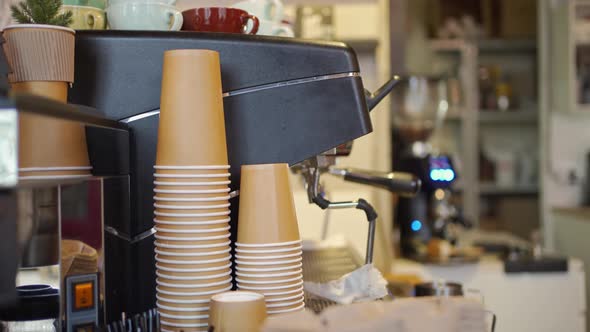 Cardboard Disposable Takeaway Coffee Cups are Stacked Near a Professional Coffee Machine in a Cafe alt
