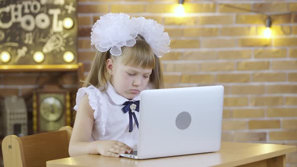 Little Girl Sits at Table and and Typing on the Laptop Keyboard on the Background of a School Class alt