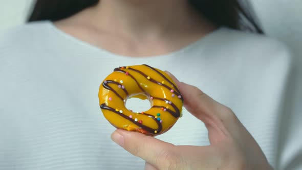 A Woman Dressed in White Clothes Holds Out an Appetizing Donut alt