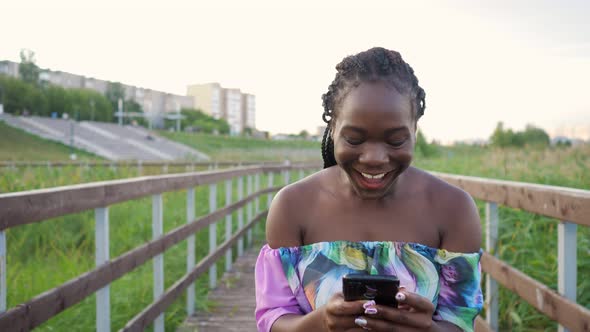 African Woman with Phone Jumping with Happiness on Wooden Bridge alt