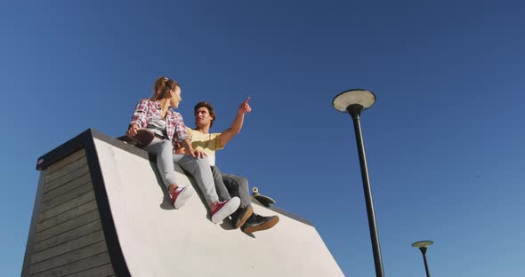 Happy caucasian woman and man friends wearing face mask, sitting and pointing something in distance alt