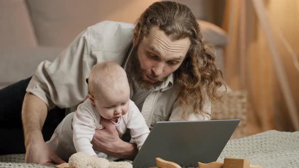 Caucasian Bearded Father with Infant Newborn Uses Laptop Internet Online Video Call Conference Chat alt