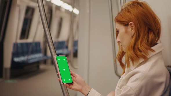 Side view female watching at green screen phone in subway train. alt