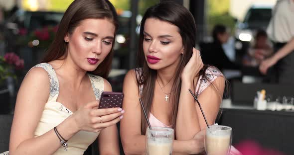 Two Beautiful Girls Serfing Internet in the Summer Cafe and They Are Surprised