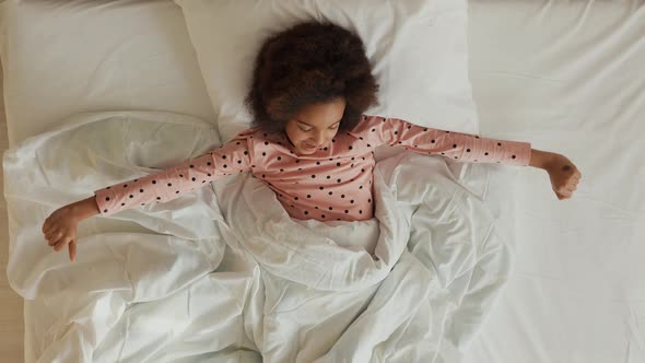 Top View of a Little Sleeping African American Girl Waking Up Stretching and Yawning alt