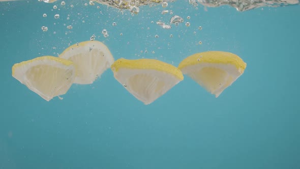 Slow Motion of Falling Lemon Slices Into Splashing Water on Blue Background alt