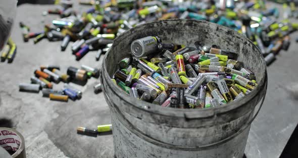 A Full Bucket of Used Batteries Amid Scattered Piles of Others