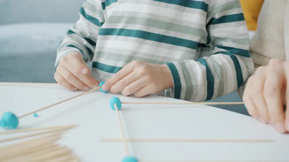Closeup of Hands Adult and Child Doing Craft with Wooden Sticks and Play Dough at Home alt