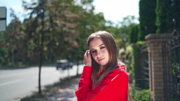 Lovely girl in red dress. Beautiful young model is standing outdoors and posing on camera. alt