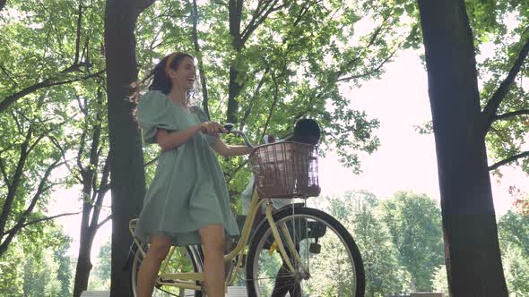 Young Mixed Race Couple Walks Through the Park with a Bicycle and Laughs on a Sunny Summer Morning alt