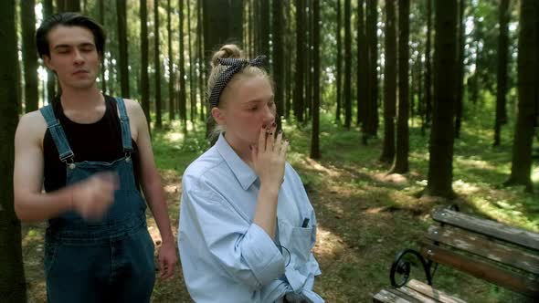 A Girl in a Blue Shirt and a Guy in a Denim Jumpsuit Stand in the Woods