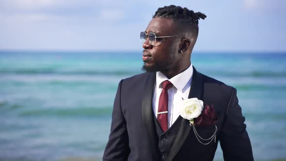 Handsome African American Man in Sunglasses and Elegant Formal Suit with Boutonniere Standing at alt