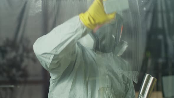 A Concentrated Man in a Respirator and a White Protective Suit Washes the Window alt
