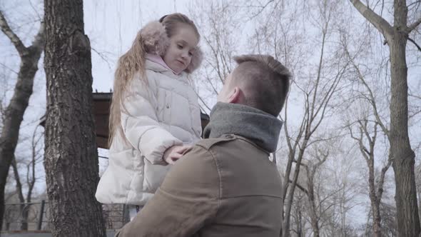 Joyful Little Girl Talking with Young Father in Park and Smiling. Portrait of Brunette Curly-haired alt