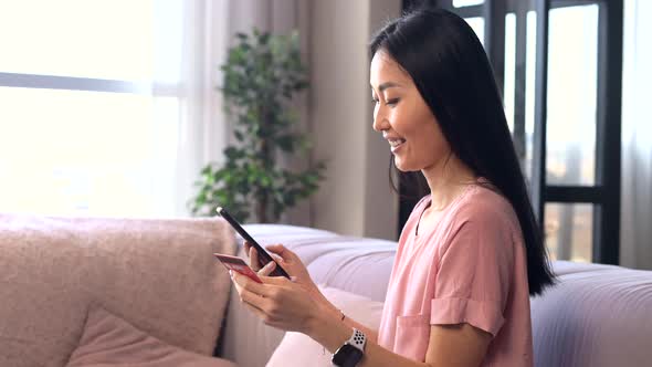 An Attractive Young Asian Woman is Using a Smartphone for Shopping Online alt