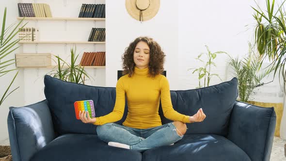Young Woman Meditating with Trendy Pop Toy in Lotus Pose at Home alt