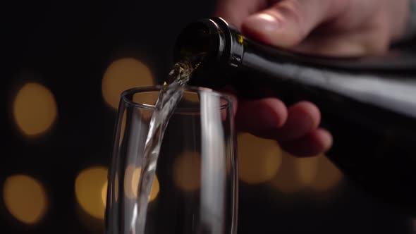Close-up of the Bartender Pouring Champagne Into a Glass on a Black Background, the Glass Has a Lot