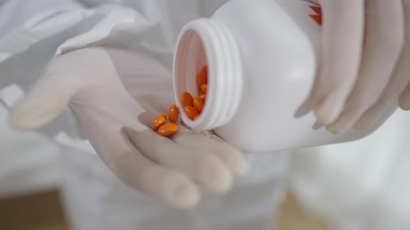 Closeup of Female Hands in White Gloves Pouring Orange Pills From Container alt