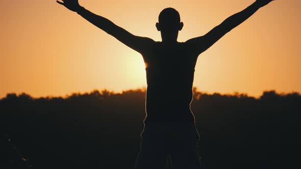 Silhouette of Young Man Against Sunset Raising Hands Sides and Up. Slow Motion alt