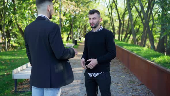Portrait of Handsome Bearded Young Man Talking with Friend Standing in City Park on Summer Spring alt