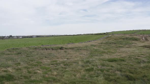 Aerial rises from cliff face to reveal green agricultural pasture land alt