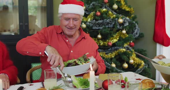 Happy caucasian senior man in santa hat serving himself food, at christmas dinner table with friends alt