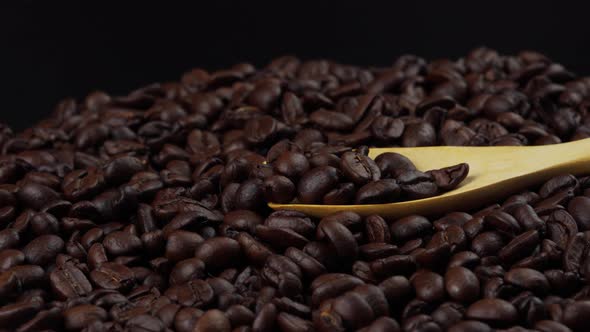 roasted coffee beans with wooden spoon rotating, seeds of coffee on black background