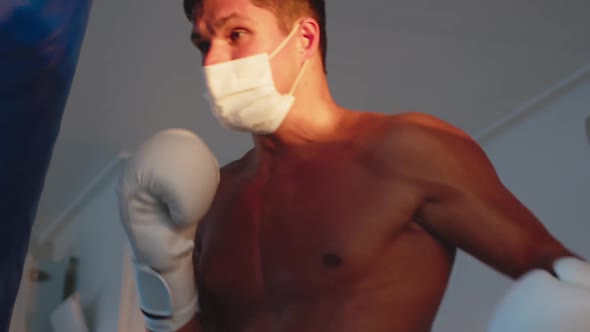 Muscled Young Man Wearing Face Mask for Boxing Workout Punching Bag Outdoor