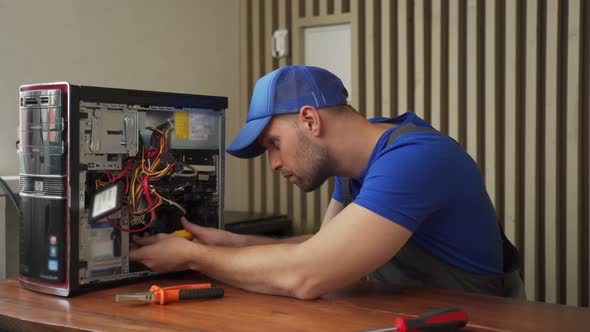 Man in Tshirt Repairs Computer System Unit with Screwdriver alt