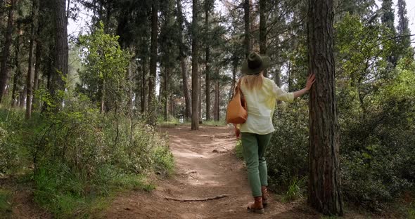 Back view of traveler woman with backpack walking in the forest. alt