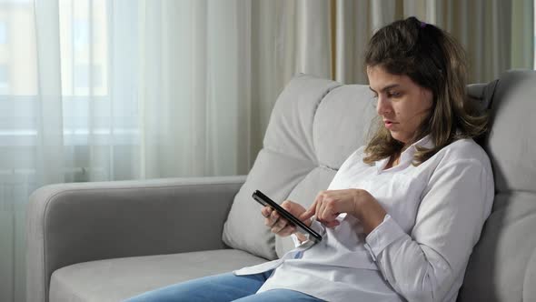 Disabled Woman Hardly Uses Mobile Phone Sitting on Sofa alt