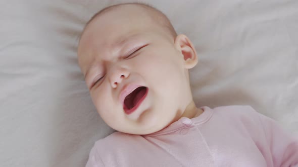 A Baby in Lies on the Bed and Cries. Child Is Upset and Crying. alt