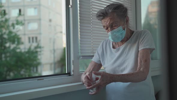 Old Woman 90 Years Wearing Face Mask Use Alcohol Spray Protect Covid 19 Standing By Window in alt