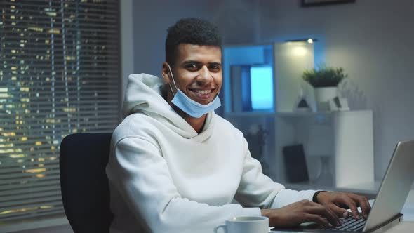 Handsome Black Man with Medical Mask Smiling To the Camera While Working Home alt