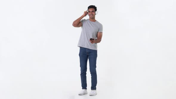 Handsome Indian man holding mobile phone in hand dancing while listening to the music on headphones