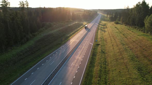 Heavy semi-trailer truck drives through beautiful terrain through the summer woods at dawn. alt