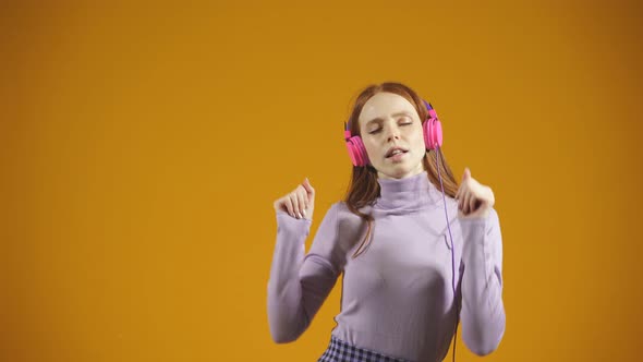 Studio Video of a Redhaired Woman with Long Loose Hair She Listens to Music in Headphones with Her