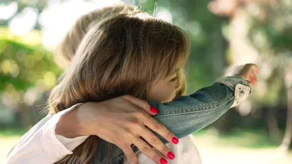 Side View Happy Little Daughter Hugging Young Mother in Sunshine Outdoors alt