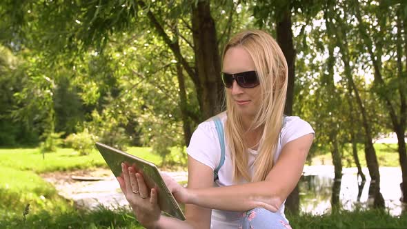 Young Woman Sitting in Park with Tablet Computer, Slow Motion. alt