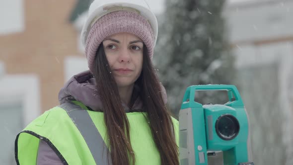 Closeup Portrait of Confident Female Surveyor Standing at Theodolite Gesturing on Winter Day alt